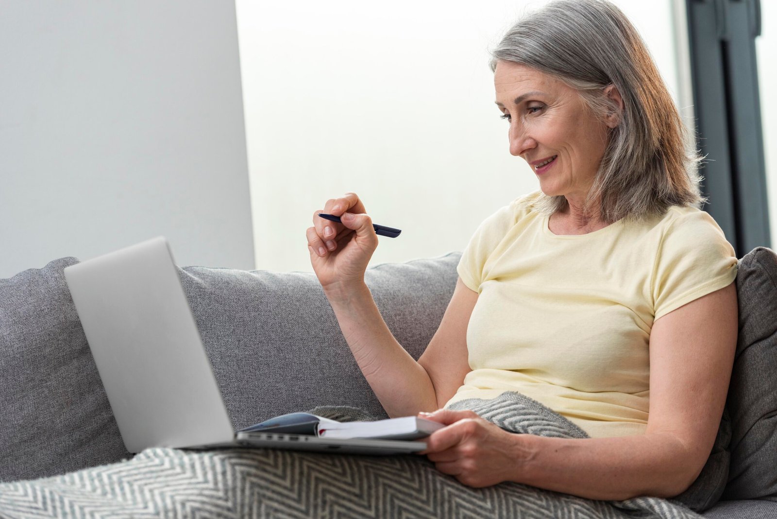 senior-woman-home-couch-using-laptop-taking-notes